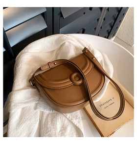 Detailed close-up of brown leather saddle bag with C-shaped buckle on a white surface