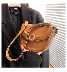 Detail of tan leather saddle bag featuring a decorative D-buckle and gold metal rivets
