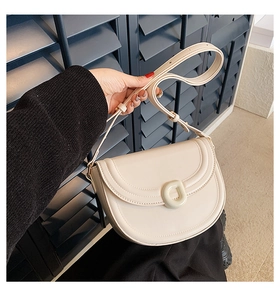 Detail of a beige leather saddle bag featuring a round decorative buckle and adjustable strap