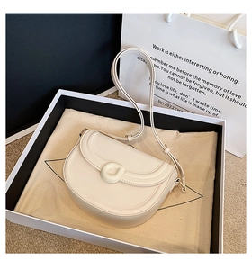 Close-up of cream saddle bag with leather texture and D-buckle in a gift box