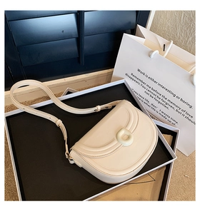 Detail view of a beige minimalist saddle bag inside a high-end black and white gift box