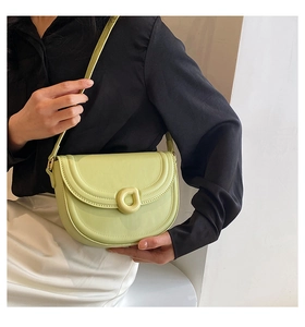 Detail of avocado green saddle bag with D-ring buckle worn by a model in soft lighting