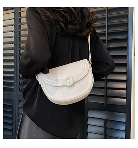 Model wearing a cream saddle bag with a D-ring buckle and elegant curved stitching