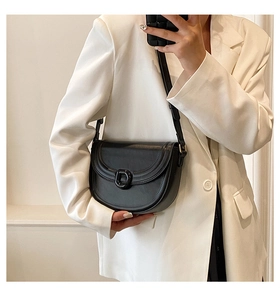 Detail of a black leather saddle bag with a minimalist buckle worn on a white blazer
