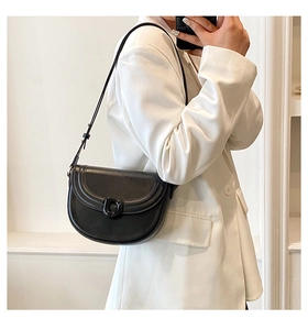 Detail of a minimalist black leather saddle bag styled on a white blazer outfit