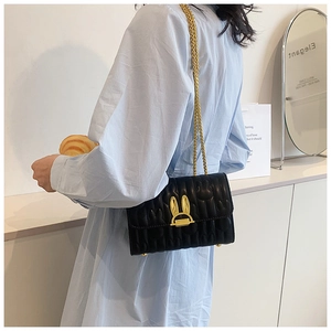 Detail of a black quilted leather crossbody bag with a gold rabbit ear lock and chain strap