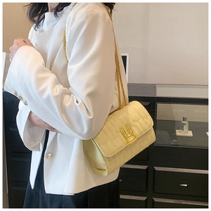 Detail of light yellow quilted bag with golden rabbit buckle and chain strap on a model