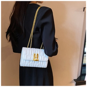 Close-up of white quilted shoulder bag with golden rabbit-shaped metal lock and chain