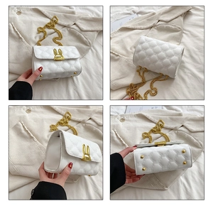 Detail view of white quilted crossbody bag with gold rabbit clasp and metal chain straps