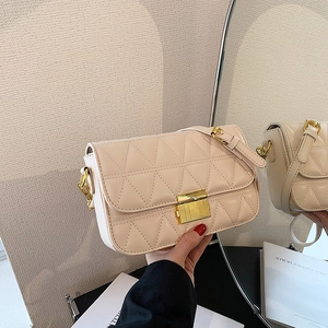 Quilted cream crossbody bag with triangle stitching and golden clasp shown in mirror