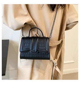 Detail of crocodile embossed black crossbody bag with chain strap styled with a beige coat