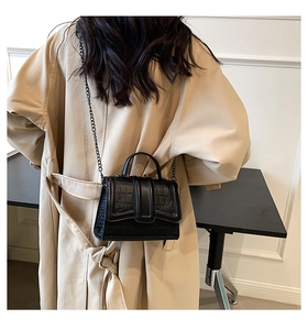 Detail of black crossbody bag with faux crocodile pattern and metal chain shoulder strap