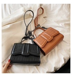 Detail view of crocodile pattern textures on black and brown shoulder bags with metal chains