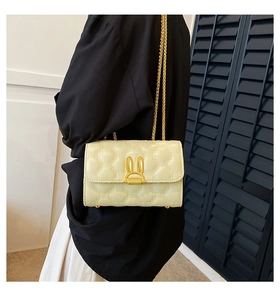 Detail of cream quilted crossbody bag with a golden rabbit-shaped lock and chain strap