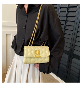 Detail of yellow heart-quilted crossbody bag with golden rabbit-ear clasp on white skirt