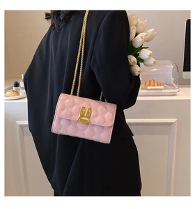 Detail of pink quilted shoulder bag featuring gold rabbit ear metal buckle and chain strap
