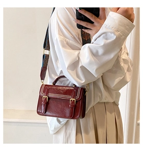 Détail d'un sac bandoulière bordeaux avec perles blanches et boucles dorées sur le modèle