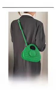 Fashionable green crocodile-patterned handbag with round hollow handle shown on a grey suit