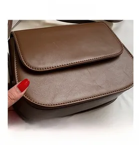 Macro detail of the dark brown leather flap closure on a stylish crossbody square bag