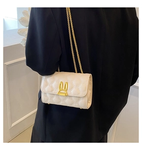 Detail shot of white quilted chain bag with gold rabbit clasp on black blazer