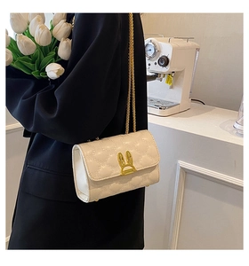 Quilted beige shoulder bag with a gold rabbit buckle shown worn by a model