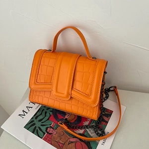 Orange croc-embossed top handle handbag with dark gunmetal chain strap on a white table