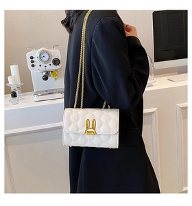 Detail of white quilted crossbody bag featuring a golden rabbit-ear clasp and chain strap