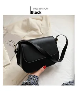 Detail of a minimalist black leather crossbody bag with metallic buckle on white background