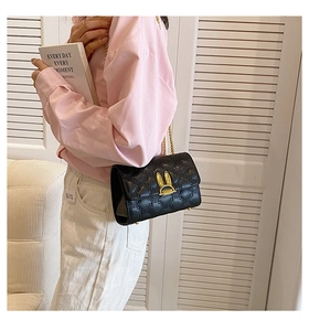 Detail of black quilted chain bag featuring a gold rabbit ear lock on a white background