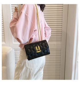 Detail of quilted black shoulder bag featuring golden bunny clasp and chain strap