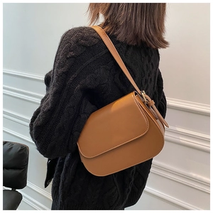 Close-up of a caramel brown leather flap bag with adjustable strap on a model