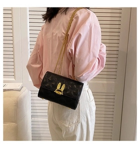 Close-up of quilted black crossbody bag with golden rabbit ear lock and metal chain strap