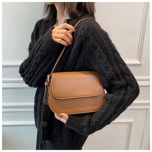 Close-up of caramel brown leather crossbody bag worn by a model in a black cardigan
