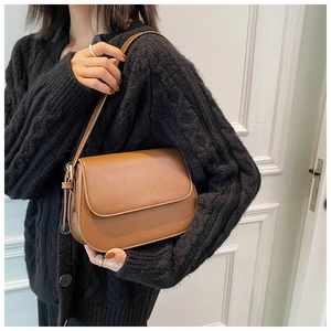 Brown leather crossbody bag detail on a model wearing a black cable knit sweater
