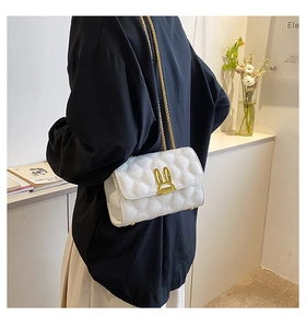 Detail of white quilted crossbody bag featuring a unique golden bunny ear twist lock