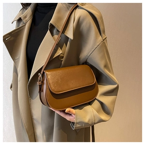 Detail of dark brown faux leather saddle bag with adjustable strap worn with a beige coat