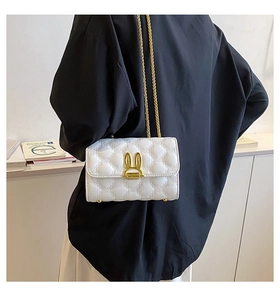 Detail of white quilted crossbody bag featuring a golden rabbit ear metal clasp and chain