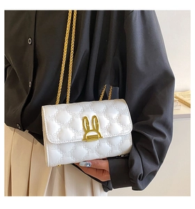 Close-up of white quilted crossbody bag with gold bunny ear clasp and chain strap
