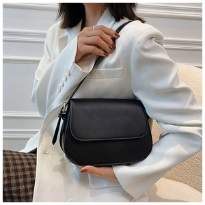 Model wearing a black matte leather crossbody bag with a white suit and plaid skirt
