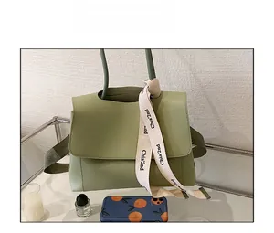 Detailed macro of a pea green matte leather tote with a silk scarf tied on the handle