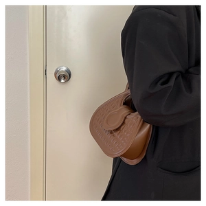 Brown leather half-moon shoulder bag with geometric embossed texture worn by a model