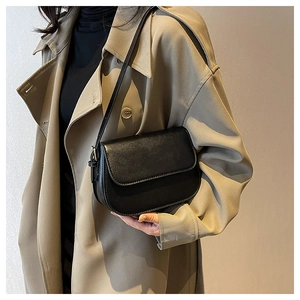 Classic black leather saddle bag shown on model wearing a beige trench coat