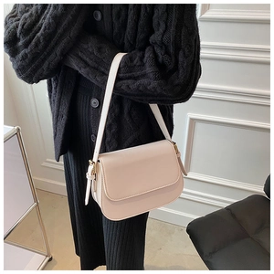 Detail of light beige crossbody bag with gold buckle on a black knit cardigan