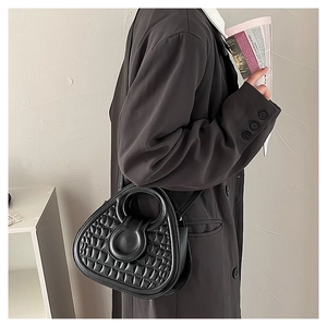 Close-up of black triangle handbag with crocodile pattern worn with a brown blazer