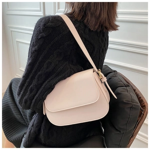 Detail of elegant beige saddle bag with gold buckle on a model in black outfit