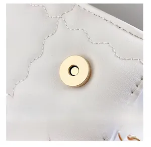 Detail einer runden goldenen Magnetschnalle an einer weißen gesteppten Ledertasche