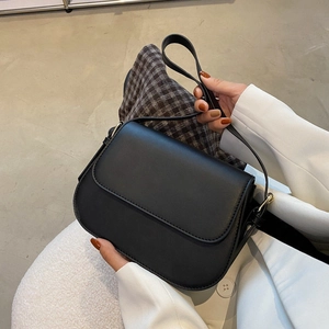 Detail of a chic black flap crossbody bag with gold hardware held by a model