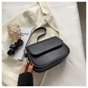 Detail view of a black flap crossbody bag with adjustable straps on a beige blazer