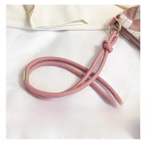 Detail of pink knotted leather strap and gold metal hardware on checkered bag