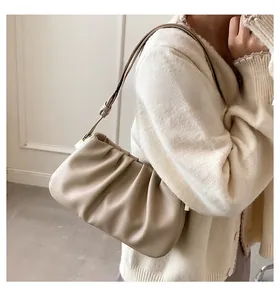 Détail du sac à bandoulière plissé beige avec garnitures dorées porté par un modèle